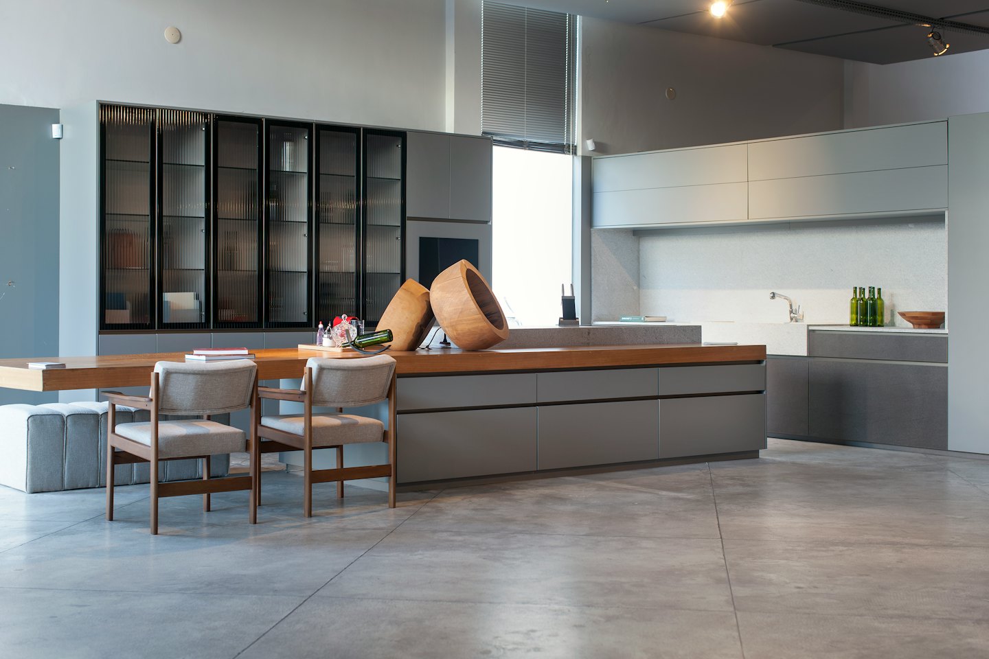 Modern kitchen showroom featuring grey cabinets and a wooden island.