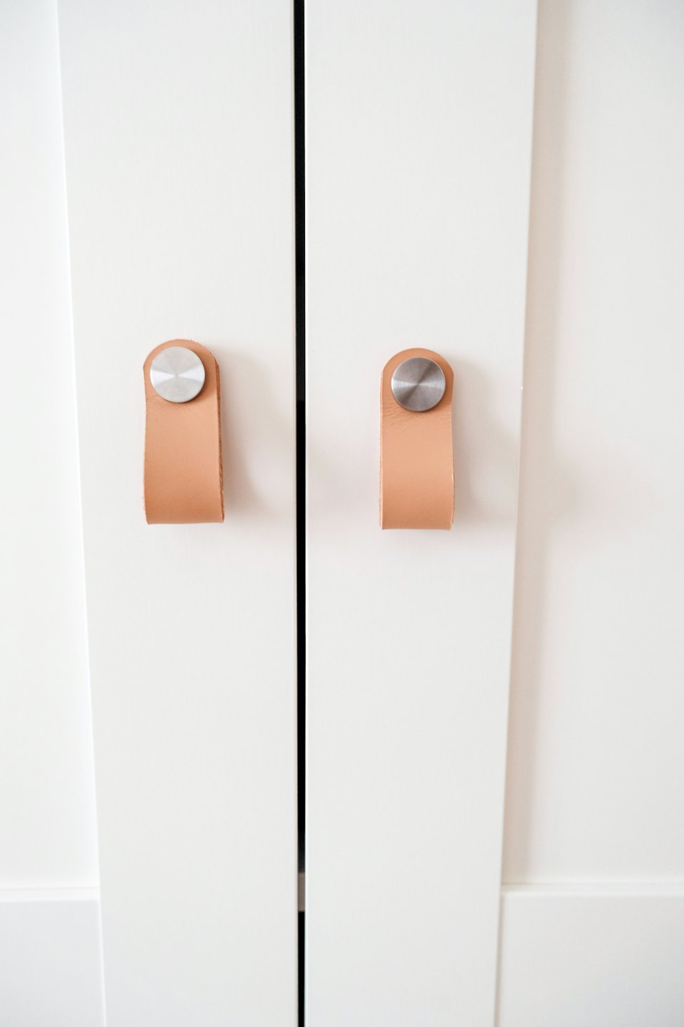 Two white cabinet doors with modern leather pull handles.