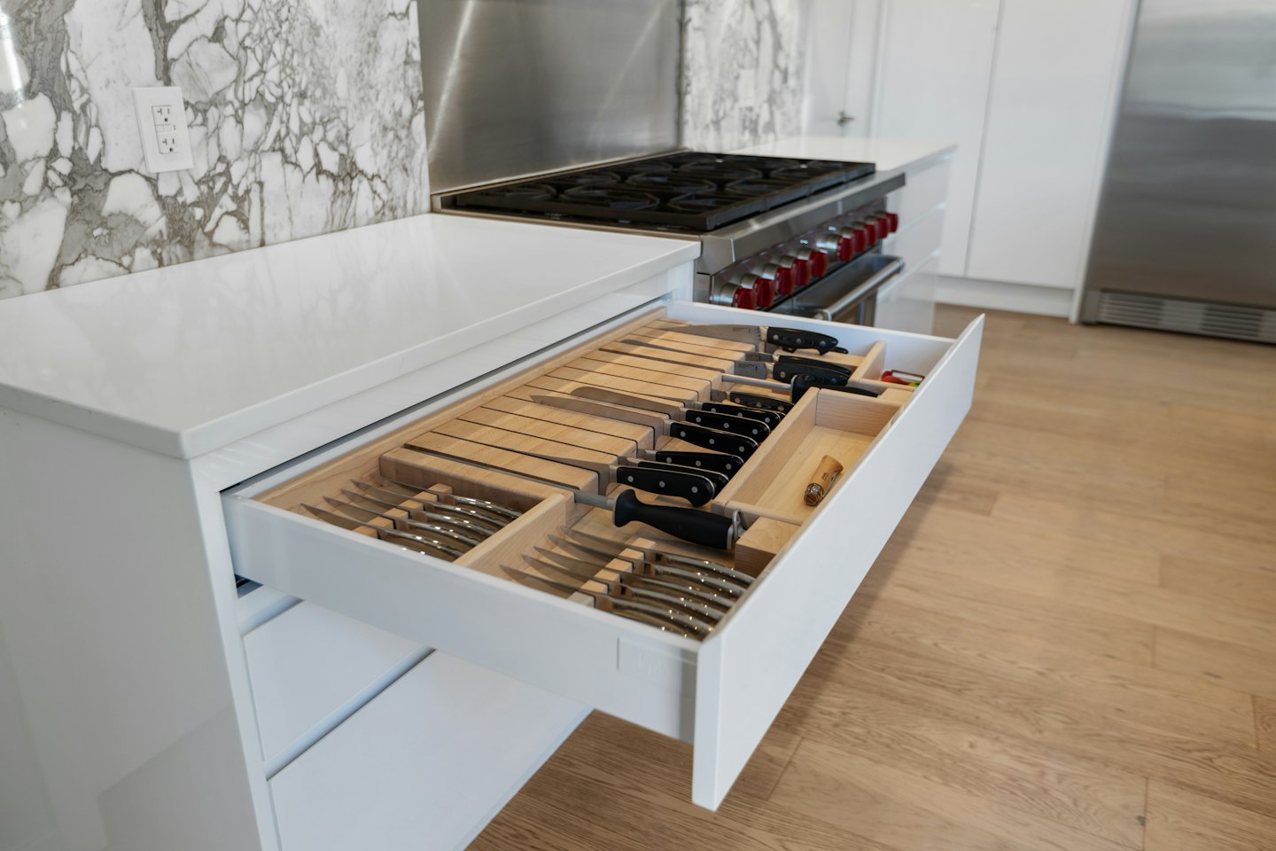 Organized cutlery and knives in a white kitchen cabinet drawer.
